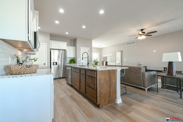 kitchen featuring appliances with stainless steel finishes, an island with sink, sink, white cabinets, and light hardwood / wood-style flooring