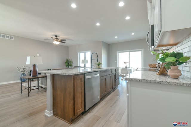 kitchen featuring sink, a center island with sink, appliances with stainless steel finishes, light stone countertops, and light hardwood / wood-style floors