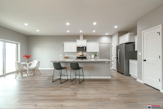 kitchen featuring white cabinetry, stainless steel appliances, an island with sink, and light wood-type flooring