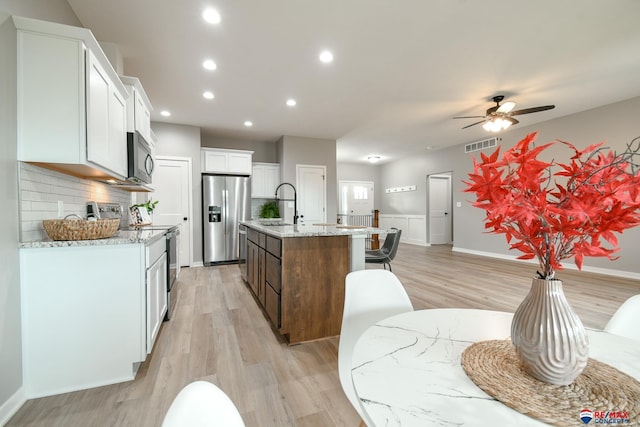 kitchen with white cabinetry, appliances with stainless steel finishes, a kitchen island with sink, and backsplash