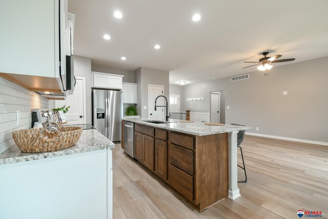 kitchen with sink, backsplash, stainless steel appliances, light stone countertops, and a center island with sink