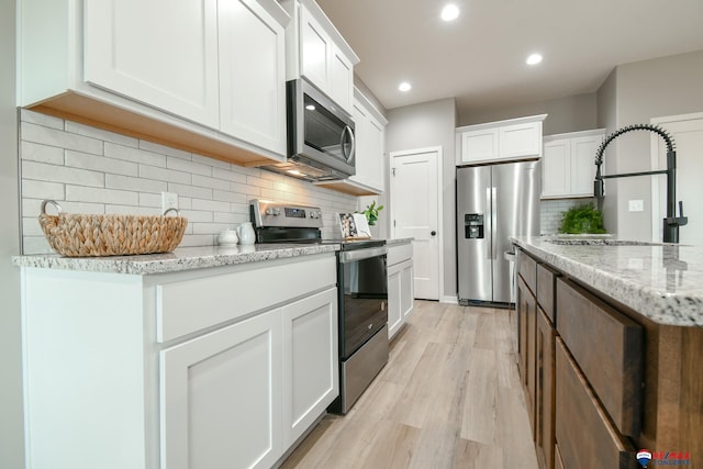 kitchen with sink, white cabinetry, backsplash, stainless steel appliances, and light stone countertops