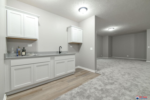 interior space featuring white cabinetry, sink, light carpet, and a textured ceiling