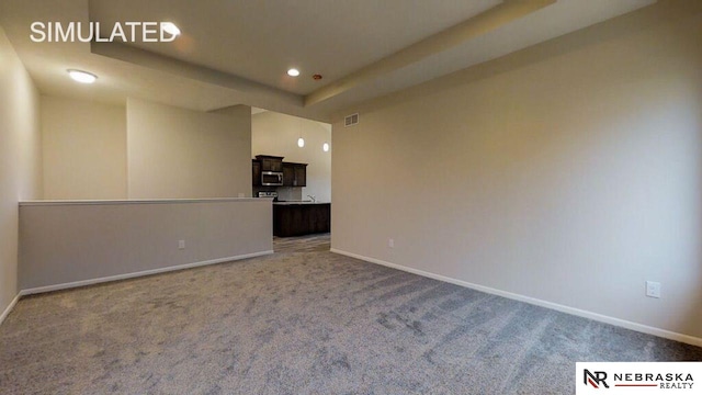 unfurnished living room featuring a tray ceiling and carpet flooring