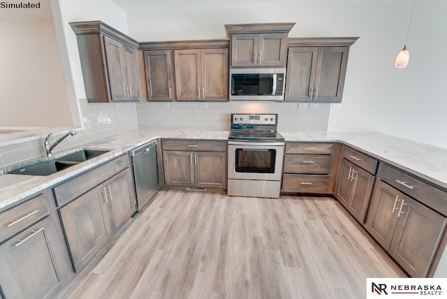 kitchen with pendant lighting, appliances with stainless steel finishes, light stone countertops, and sink