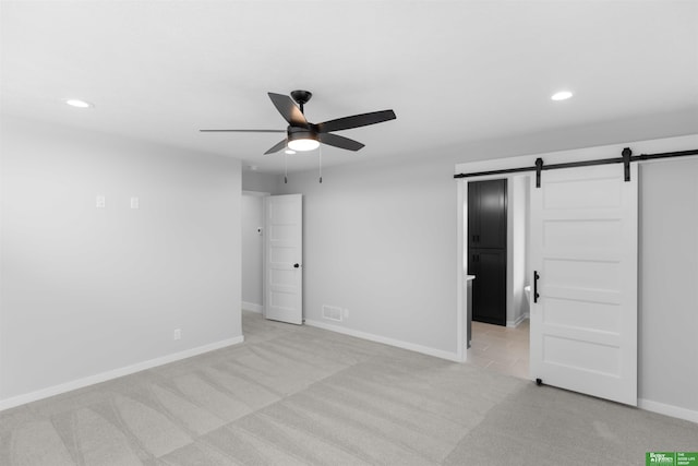 unfurnished bedroom featuring a barn door, light carpet, and ceiling fan