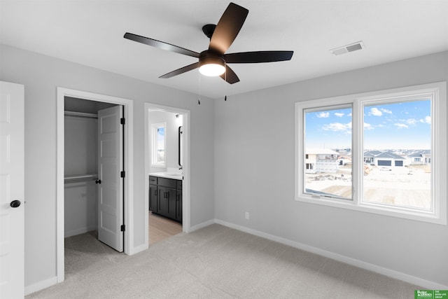 unfurnished bedroom featuring ceiling fan, light carpet, ensuite bath, and a closet