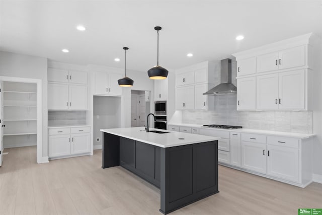 kitchen featuring a center island with sink, white cabinetry, tasteful backsplash, and wall chimney range hood