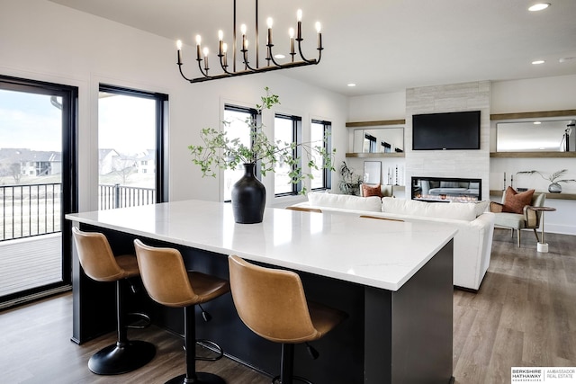 kitchen with a breakfast bar area, wood-type flooring, a kitchen island, pendant lighting, and a tiled fireplace