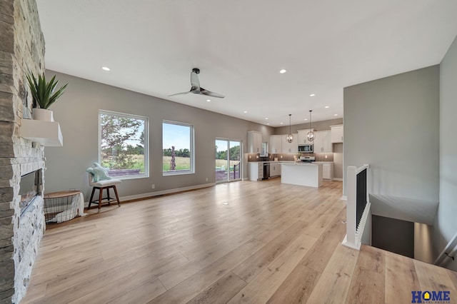 unfurnished living room with ceiling fan, a stone fireplace, and light hardwood / wood-style flooring