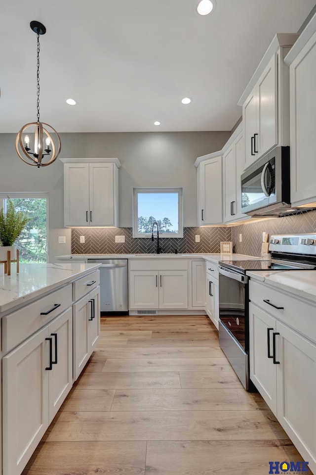 kitchen featuring sink, white cabinetry, light hardwood / wood-style flooring, appliances with stainless steel finishes, and pendant lighting