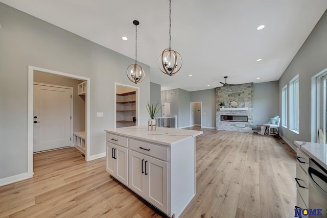 kitchen featuring pendant lighting, light hardwood / wood-style flooring, white cabinetry, light stone counters, and a fireplace