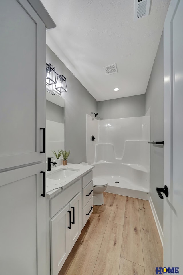 bathroom with walk in shower, toilet, wood-type flooring, a textured ceiling, and vanity