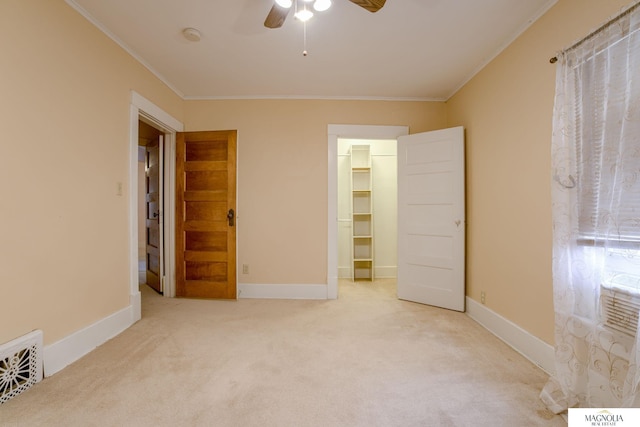 unfurnished bedroom with ornamental molding, a walk in closet, light colored carpet, ceiling fan, and a closet