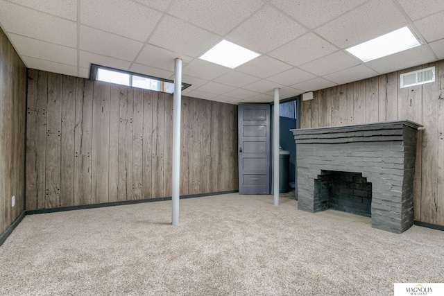 basement featuring wood walls, a fireplace, light carpet, and a drop ceiling