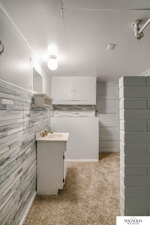 interior space featuring wood walls, sink, light carpet, and white cabinets