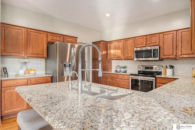 kitchen featuring light stone counters, sink, a breakfast bar area, and appliances with stainless steel finishes