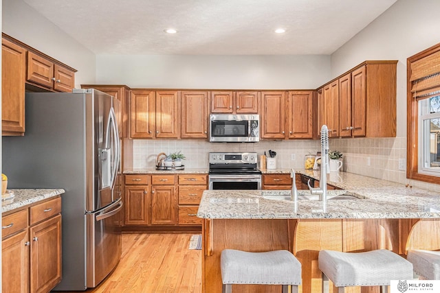 kitchen featuring appliances with stainless steel finishes, tasteful backsplash, a breakfast bar area, light hardwood / wood-style floors, and light stone countertops