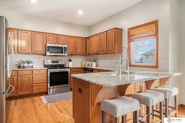 kitchen with appliances with stainless steel finishes, a breakfast bar, light stone counters, kitchen peninsula, and light wood-type flooring