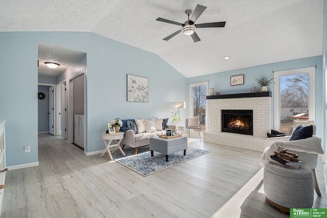 living room with ceiling fan, lofted ceiling, a fireplace, and light wood-type flooring