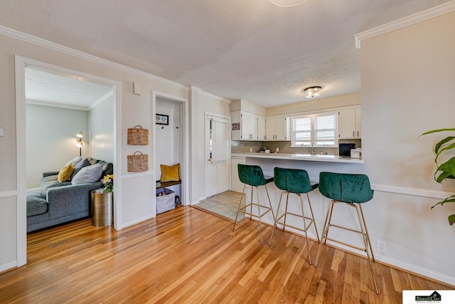 kitchen featuring light hardwood / wood-style flooring, a breakfast bar, white cabinetry, backsplash, and kitchen peninsula