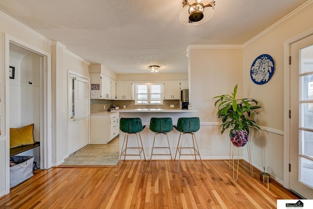 kitchen featuring tasteful backsplash, kitchen peninsula, white cabinets, and light wood-type flooring