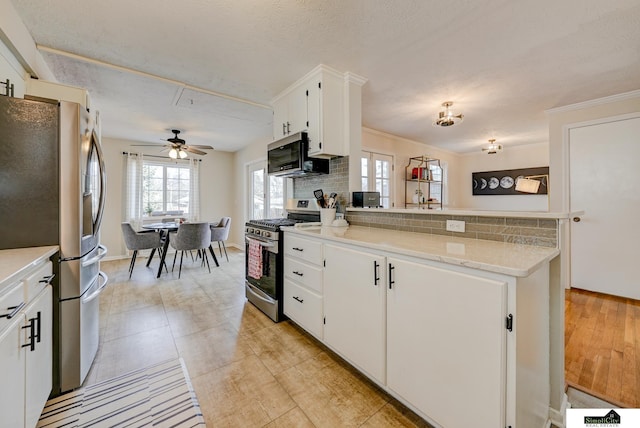 kitchen with appliances with stainless steel finishes, ornamental molding, white cabinets, decorative backsplash, and kitchen peninsula