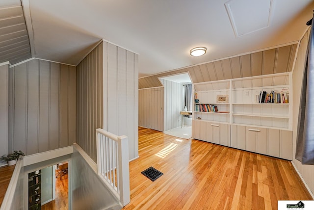 bonus room featuring lofted ceiling, built in features, light hardwood / wood-style floors, and wood walls