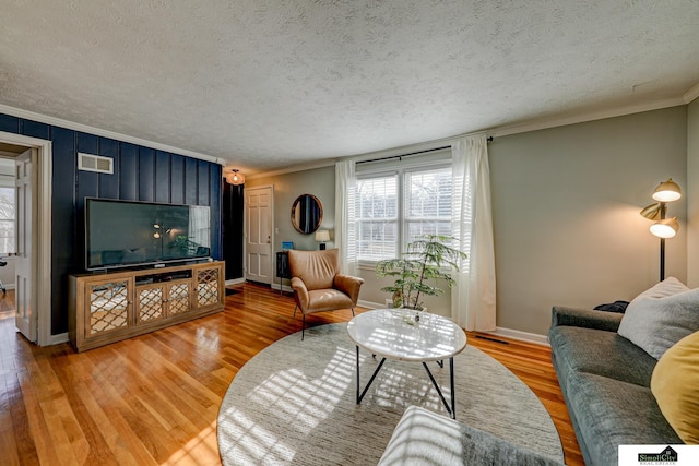 living room with wood-type flooring, ornamental molding, and a textured ceiling