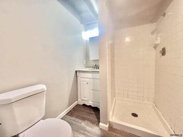 bathroom with a tile shower, vanity, wood-type flooring, and toilet