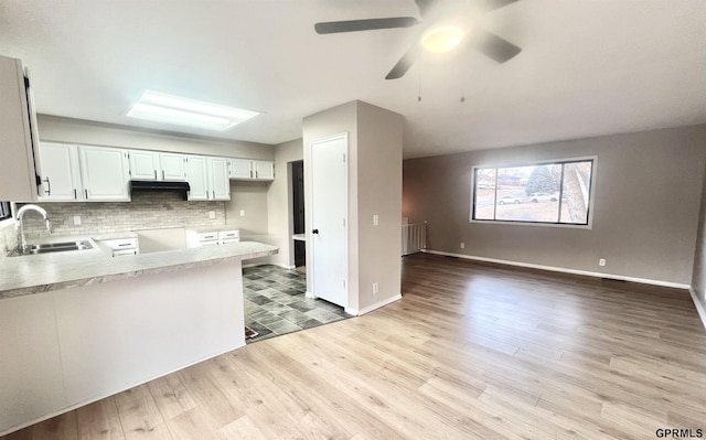 kitchen featuring a skylight, white cabinetry, sink, backsplash, and kitchen peninsula