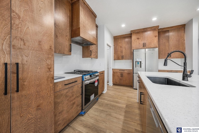 kitchen featuring sink, light stone counters, custom range hood, stainless steel appliances, and light hardwood / wood-style floors