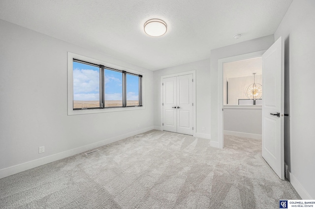 unfurnished bedroom featuring light carpet, a textured ceiling, a closet, and a chandelier