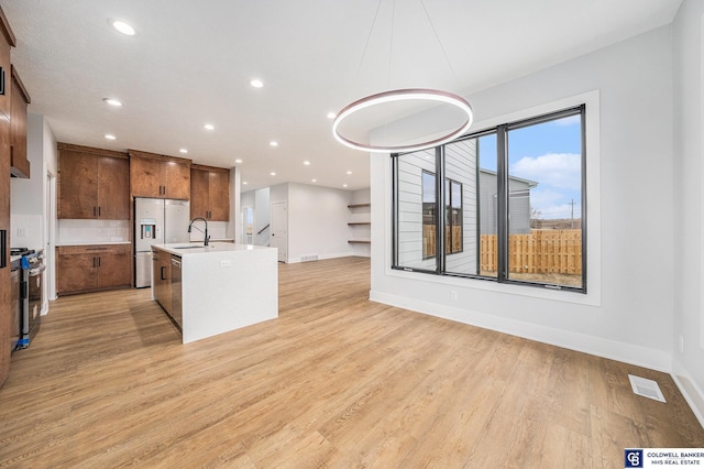 kitchen featuring sink, light hardwood / wood-style flooring, hanging light fixtures, stainless steel appliances, and a center island with sink