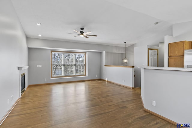 unfurnished living room featuring dark hardwood / wood-style flooring, vaulted ceiling, and ceiling fan