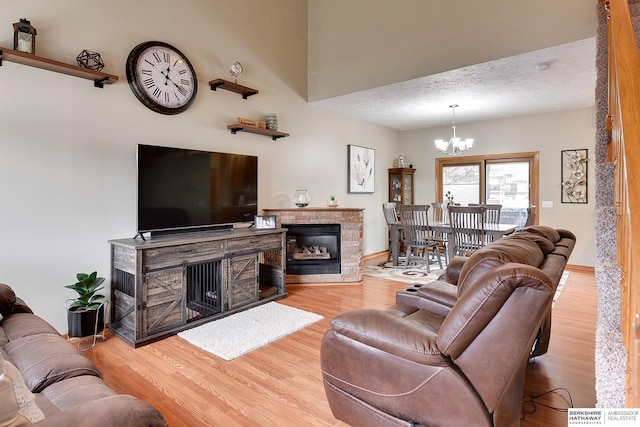 living room featuring wood-type flooring, a stone fireplace, a chandelier, and a textured ceiling