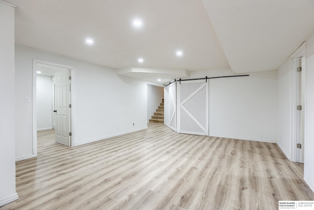 basement with a barn door and light hardwood / wood-style floors