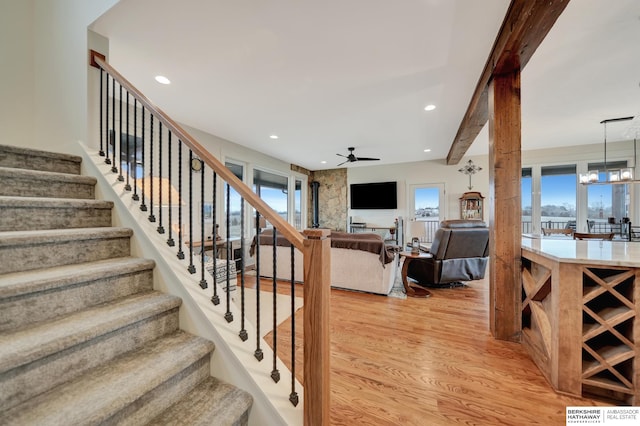 staircase with beam ceiling, ceiling fan with notable chandelier, and wood-type flooring