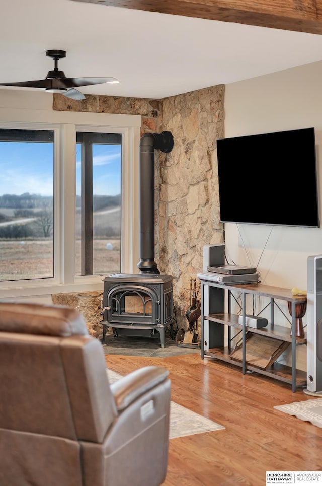 living room featuring wood-type flooring, a wood stove, and ceiling fan
