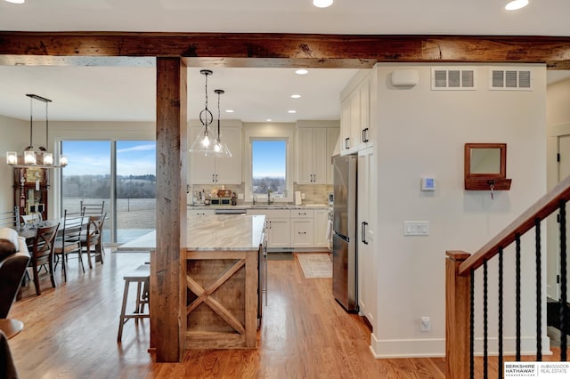 kitchen with white cabinetry, beam ceiling, light stone countertops, and a wealth of natural light