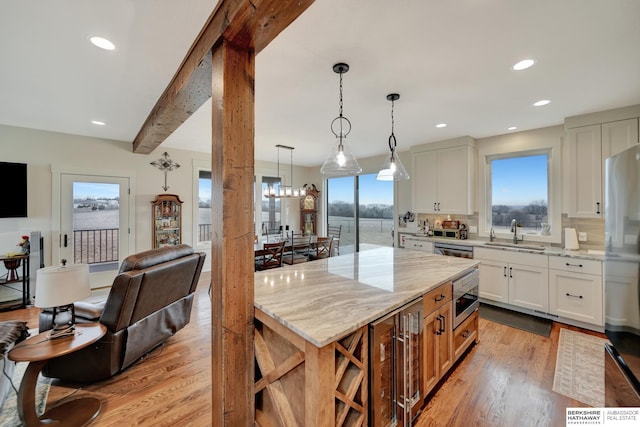 kitchen featuring white cabinetry, hanging light fixtures, stainless steel appliances, light stone countertops, and light hardwood / wood-style flooring