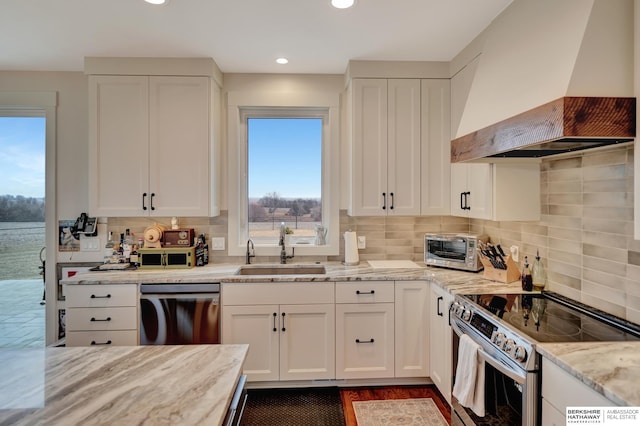 kitchen with custom exhaust hood, white cabinetry, sink, and stainless steel appliances