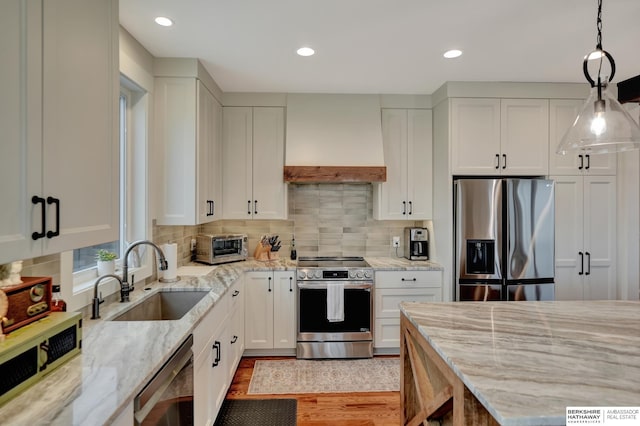 kitchen with premium range hood, white cabinetry, stainless steel appliances, and sink