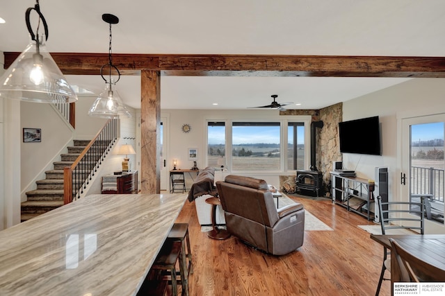 living room featuring plenty of natural light, wood-type flooring, beamed ceiling, and a wood stove