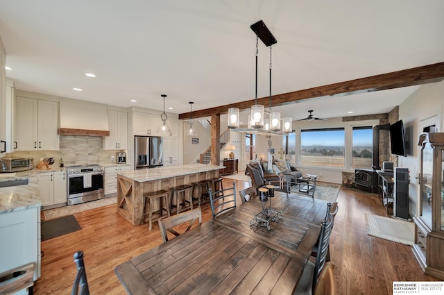dining room featuring beamed ceiling, wood-type flooring, a wood stove, and ceiling fan
