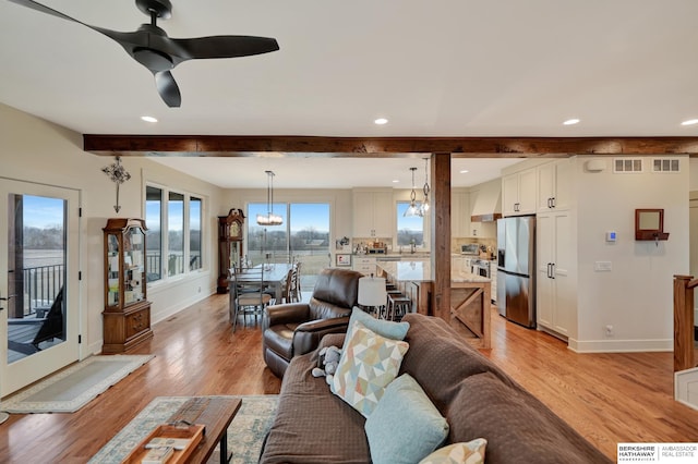 living room with sink, ceiling fan with notable chandelier, beamed ceiling, and light wood-type flooring