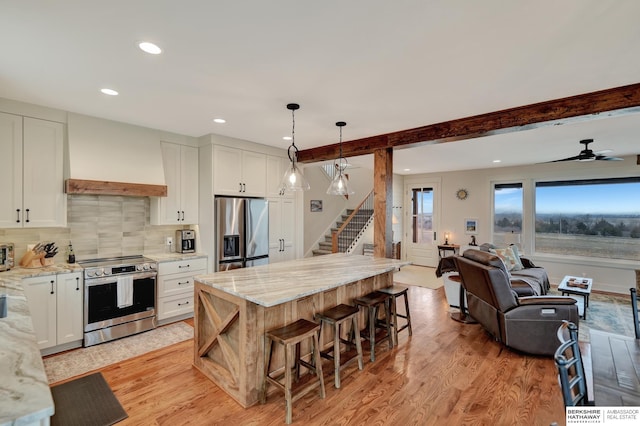 kitchen featuring premium range hood, appliances with stainless steel finishes, decorative light fixtures, white cabinetry, and light stone counters