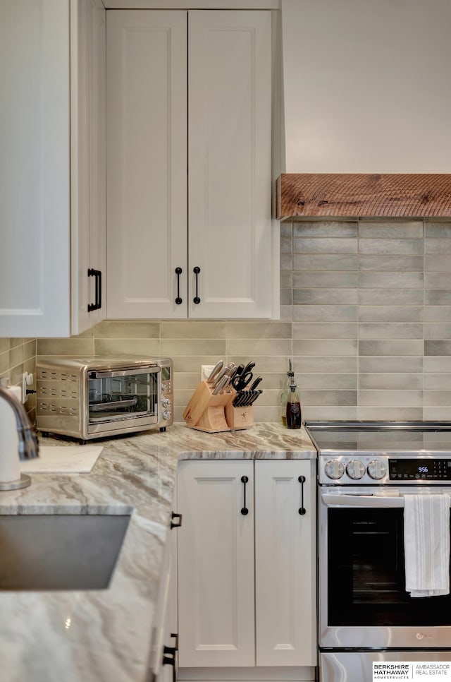 kitchen featuring premium range hood, white cabinetry, light stone countertops, stainless steel electric range oven, and decorative backsplash