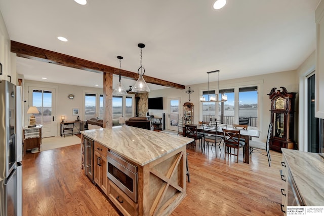 kitchen with light hardwood / wood-style flooring, appliances with stainless steel finishes, beam ceiling, light stone counters, and a kitchen island