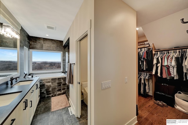 bathroom with toilet, vanity, and tiled bath